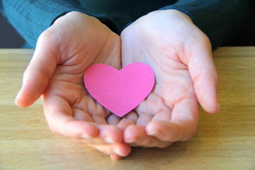 Obraz premium Pink paper heart lies in the open palms of a girl in a blue sweater