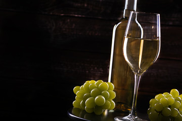 Wite wine bottle and a full glass and grapes on a table on a wooden background