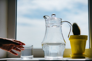 Woman's hand holding a glass of water on a windowsill