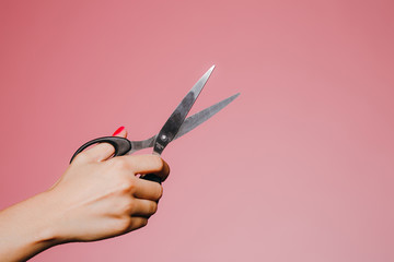 Woman's hand with the scissors isolated on pink background