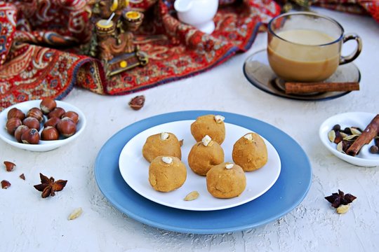 Besan laddu, Indian sweets from chickpea flour and ghee butter with hazelnuts and cardamom on a white plate on a light concrete background. Served with masala tea. Traditional Indian sweets.