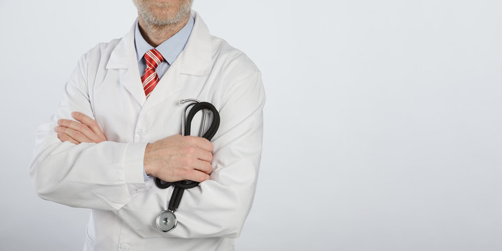 Stethoscope in hands of bearded medical doctor with arms crossed