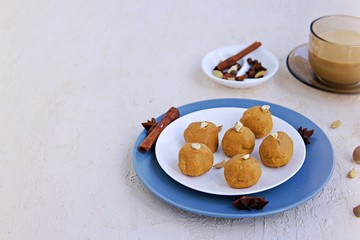 Besan laddu, Indian sweets from chickpea flour and ghee butter with hazelnuts and cardamom on a white plate on a light concrete background. Served with masala tea. Traditional Indian sweets