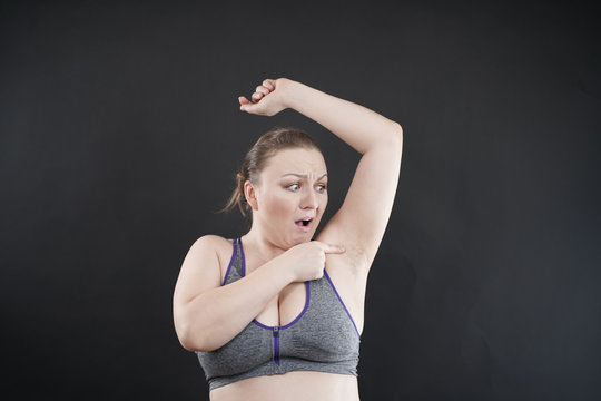 unhappy woman shows her unshaved armpit. plus size middle age woman is not happy with hair in her armpits. Caucasian girl is emotional sad and upset. black background in the photo Studio.