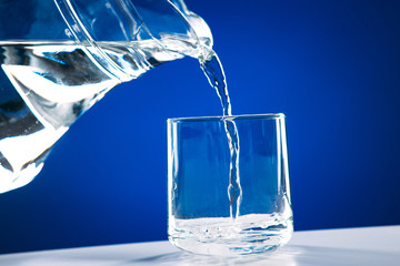 Pouring water from glass jug to glass isolated on a blue background