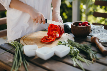 Woman's hands cutting red pepper on wooden plate. Healthy vegetarian food