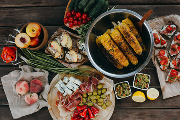 Summer picnic or BBQ food concept. Selection of vegetables, sandwiches, grilled corn and meat. Top view table scene on a wood background.