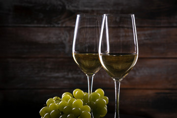 Two full white wine glasses with grapes on a table on a wooden background