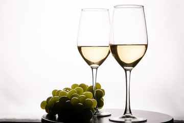 Two glasses with white wine and grapes on white background
