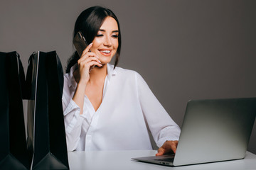 Smiling girl in a white shirt, with a laptop, and holding a credit card and a phone, preparing for...