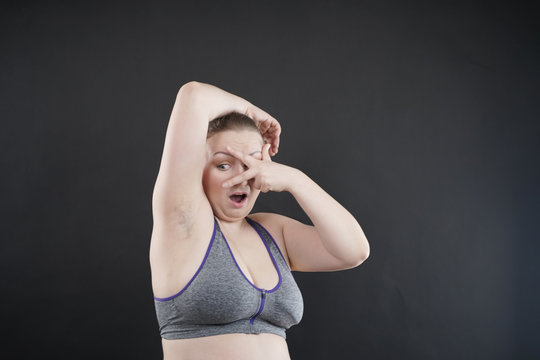 unhappy woman shows her unshaved armpit. plus size middle age woman is not happy with hair in her armpits. Caucasian girl is emotional sad and upset. black background in the photo Studio.