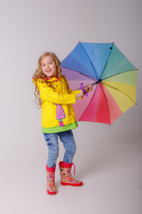 baby girl with bright umbrellas in boots on a gray background, spring