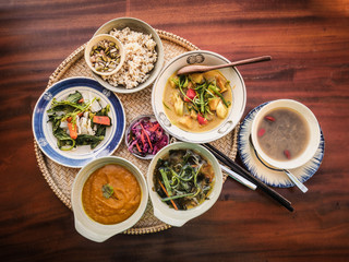 bird view of mix of vegan dishes with pumpkin soup, miso soup, blanched roots and veggies, pickle and nut, home made curry, green beans an aloe vera gruel, brown rice and seeds on a tray on table