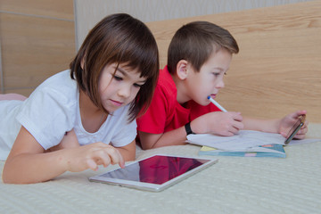 children a boy and a girl schoolchildren is engaged in lessons does tasks remotely in a notebook with a pen lies on a bed looks at a ipad