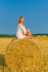 Naklejka na ściany i meble vertical portrait on a haystack of a beautiful young woman on a background of clear blue sky