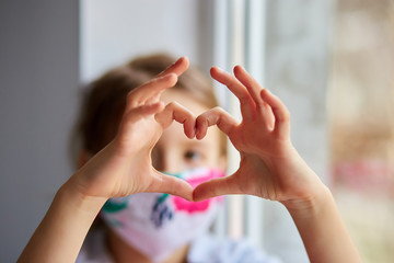 Little girl, child in mask making hearts from hands, coronavirus quarantine