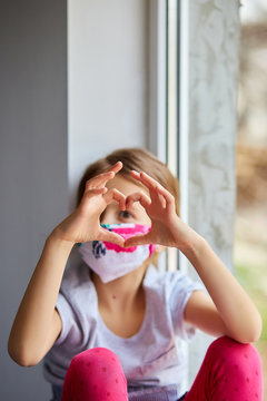 Little girl, child in mask making hearts from hands, coronavirus quarantine