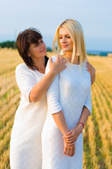 vertical portrait of a fifty year old brunette and thirty five year old blonde in white dresses