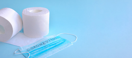 Toilet paper and a medical mask with the words CORONAVIRUS on a blue background. The concept of scarcity in quarantine. Space for advertising text, banner