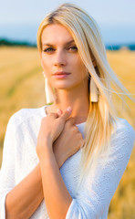 Fototapeta na wymiar vertical portrait of a beautiful blonde in a white dress on a background of a wheat field and blue sky