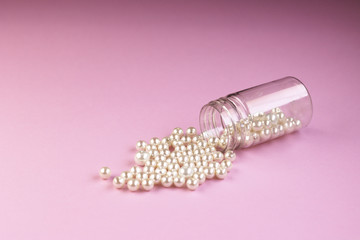 glass jar with white beads. pearls are scattered on a pink background. white decorative stones