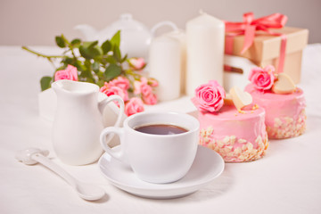 A cup of tea, pink roses and small cakes on the white table