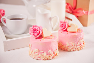 Fototapeta na wymiar A cup of tea, pink roses, gift box and small cakes on the white table. Romantic concept.