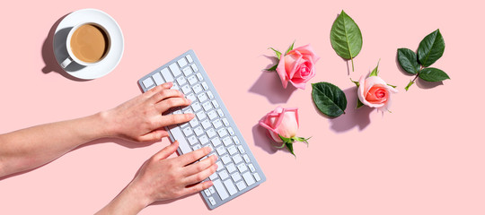Woman using computer keyboard with pink roses - flat lay