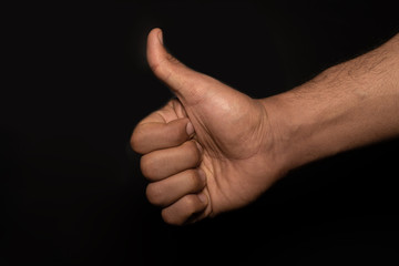Male strong hand showing thumb up gesture. Closeup front view photograph on a black studio...