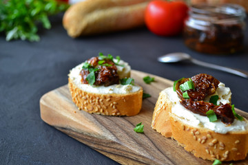 French baguette with cream cheese and dried tomatoes on a dark background.