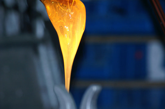 Strang aus geschmolzenem rot-orangenen Glas vor blauem Hintergrund