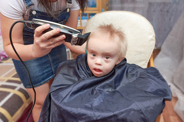 Mom cuts the blonde hair on the head of her little son with a hair clipper at home.