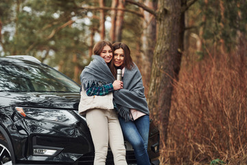 Mother and daughter standing together near modern black car outdoors in the forest