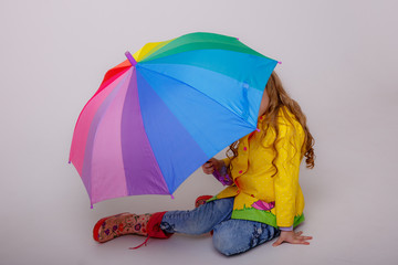 baby girl with bright umbrellas in boots on a gray background, spring