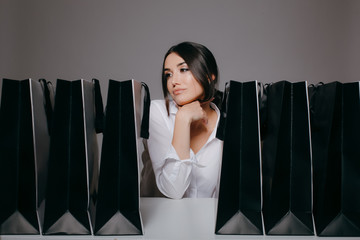 Picky rich girl with her Black Friday shopping. Lots of bags on the table. Isolated on grey