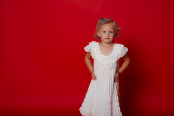 Serious cute blonde curly model girl stand posing in white dress isolated on red