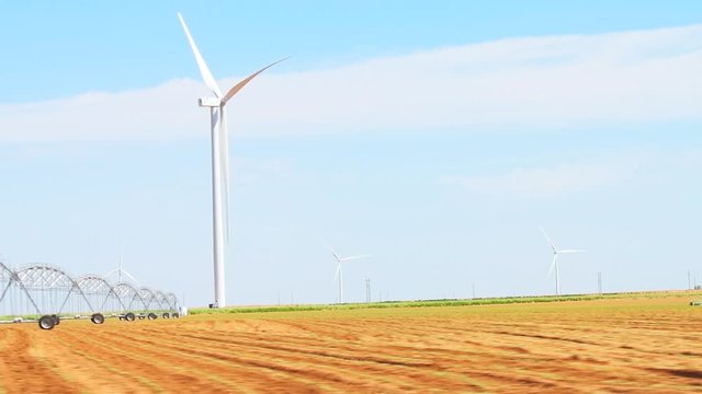 Slow motion of wind turbines at windfarm in rural farm field near Snyder or Roscoe Texas in USA isolated and sky with irrigation agricultural water pivot sprayer sprinkler system