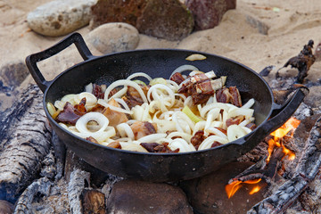 Pieces of lamb with onion are fried on the fire. As a stage in the preparation of traditional pilaf.