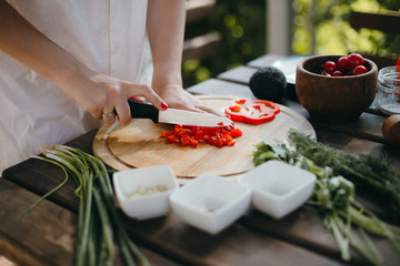 Woman's hands chopping red pepper on wooden plate. Healthy vegetarian food