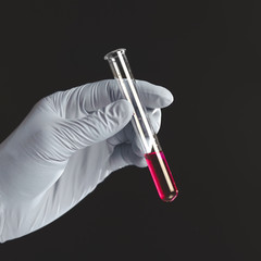 Hand holding red liquid in test tube close up isolated on black background.