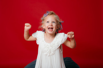 Happy young blonde curly model girl smiling jumping in white dress isolated on red