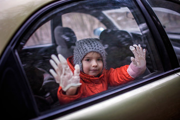 Little boy wearing respirator mask and medical gloves looking through a car window, stay safe