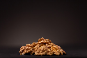 Small pile of vibrant brown walnut nuts contrasted against a dark studio background. Closeup macro low key still life.