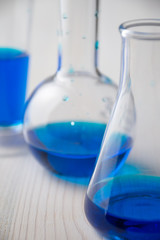 Close-up of three different glass test tubes with blue liquid and selective focus, on white wooden table, vertical