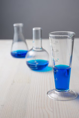 Top view of three different glass test tubes with blue liquid and selective focus, on white wooden table and gray background, vertical