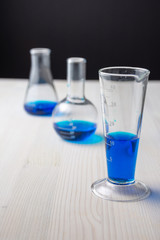 Top view of three different glass test tubes with blue liquid and selective focus, on white wooden table and black background, vertically with copy space