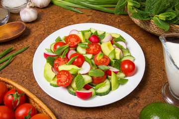 Salad of avocado, tomato, radish, cucumber and mint with yogurt sauce on a brown table. Selected focus.