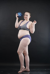 Fototapeta na wymiar Beautiful plus size woman wearing sport underweaer holds box with gift subscription to a fitness on black studio solid background.