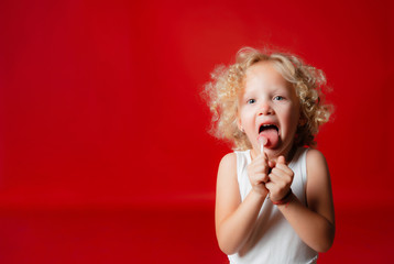 Pretty little blonde curly girl in white dress holding lollipop isolated on red