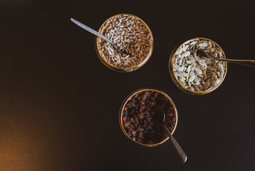 three bowls with  raisins pumpkin and sunflower seeds with spoons inside on the brown background. Blank space image.